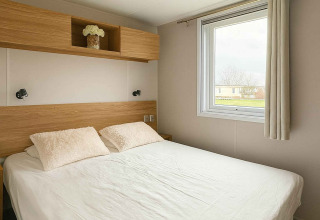 Camera da letto moderna con letto matrimoniale, finestra e mensola in legno al Vakantiehuis Celestia, Camping Papillon.
