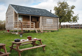 Træhytte med veranda og picnicbord på en grøn mark, BoerenBed Hollings Hill, West Midlands, Storbritannien.