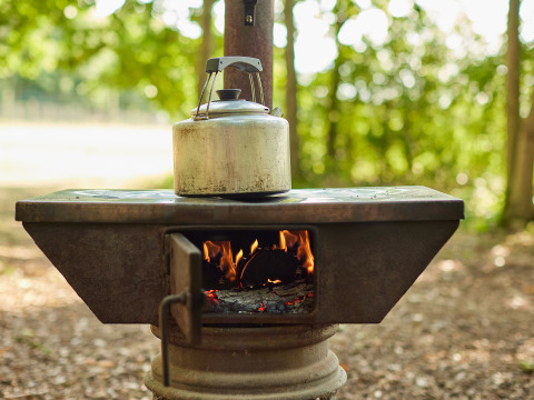 Estufa de leña tradicional con tetera encima, fuego encendido, al aire libre en BoerenBed Layer Marney Tower.
