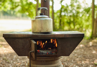 Rustic wood stove with kettle on top, burning fire, outdoors at BoerenBed Layer Marney Tower holiday park.