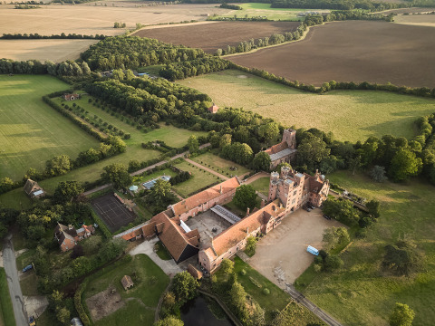 Luftfoto af BoerenBed Layer Marney Tower feriepark i det østlige England omgivet af marker og skov.