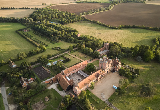 Luftfoto af BoerenBed Layer Marney Tower feriepark i det østlige England omgivet af marker og skov.