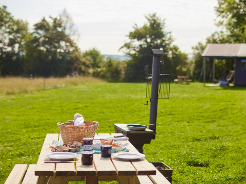 Picknicktisch mit Frühstück, Brotkorb und Tassen auf einer Wiese im BoerenBed Moor Farm Ferienpark.