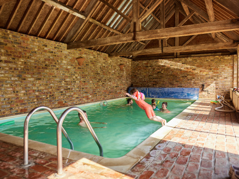 Indoor swimming pool at BoerenBed Moor Farm in South West England, with children jumping and playing.