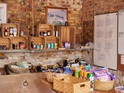 Rustic pantry at BoerenBed Moor Farm, South West England, with shelves of snacks and basic groceries on display.