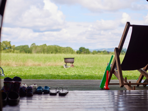 View from a tent with sandals, chair and kids' toys at a farm holiday park in South West England, UK.