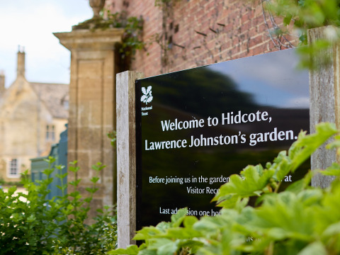 Velkommen til Hidcote, Lawrence Johnstons have, skilt foran murstensbygning og grønne planter i West Midlands, Storbritannien.
