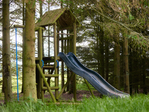 Houten speeltuin met glijbaan en klimrek tussen bomen bij BoerenBed Hidcote Manor Farm, West Midlands.