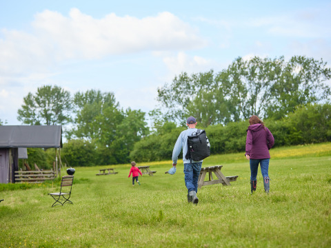 Gezin wandelt over grasveld met picknicktafels bij BoerenBed Hidcote Manor Farm vakantiepark, West Midlands, VK.