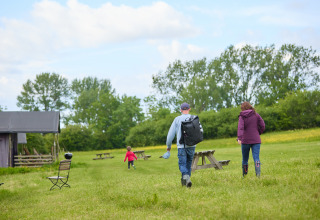 Familia caminando por césped con mesas de picnic en BoerenBed Hidcote Manor Farm, parque vacacional en West Midlands, Reino Unido.