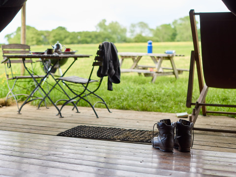 Vista desde un porche de madera con botas, mesa y sillas en Hidcote Manor Farm, West Midlands, Reino Unido.