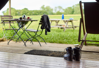 Uitzicht vanaf een houten veranda met laarzen, tafel en stoelen bij Hidcote Manor Farm, West Midlands.