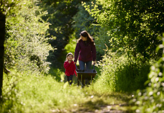 Vrouw en kind wandelen samen met een kruiwagen op een zonnig pad bij BoerenBed Hidcote Manor Farm.