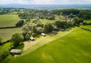 Vista aérea del parque vacacional BoerenBed Hidcote Manor Farm en West Midlands, Reino Unido, con cabañas y campo.