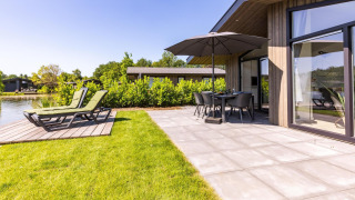 Moderne lodge Villa Waterzicht Luxe met Hottub 4 met terras, ligbedden, tuinset en uitzicht op het meer.