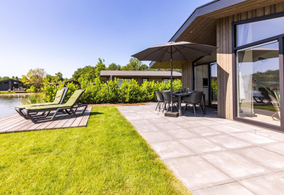Moderna Villa Waterzicht Luxe met Hottub 4 con terraza, tumbonas y vistas al lago en un día soleado.