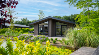 Moderne lodge Villa Waterzicht Luxe met grote ramen, terras en uitzicht op vijver met weelderige planten