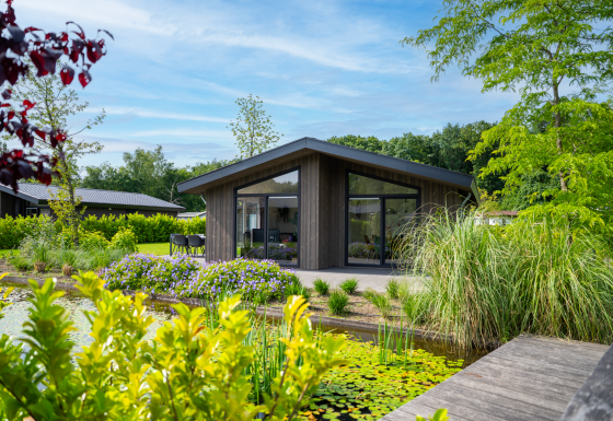 Modern lodge Villa Waterzicht Luxe with large windows, patio, and views of pond surrounded by lush plants