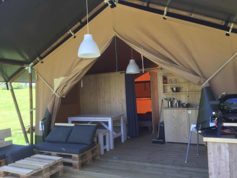 Innenansicht eines Safarizeltes mit Holzmöbeln, Sofa, Esstisch, kleiner Küche und Blick ins Freie.
