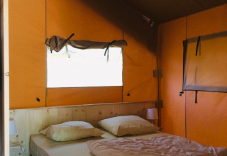 Binnenaanzicht van een safaritent met een comfortabel tweepersoonsbed, hoofdkussens en oranje muren.