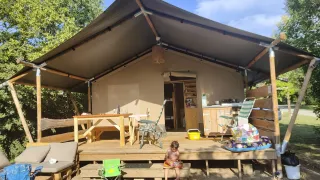 Safari telt med træveranda, spisebord og afslapningsområde, med et barn der sidder på trappen.