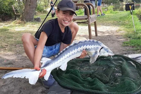 Ragazzo sorride e tiene un grosso pesce vicino a una rete al campeggio Le Paradou in Auvergne-Rhône-Alpes, Francia.