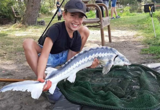 Ragazzo sorride e tiene un grosso pesce vicino a una rete al campeggio Le Paradou in Auvergne-Rhône-Alpes, Francia.