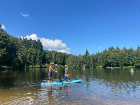 Due persone fanno paddleboarding su un lago tranquillo al campeggio Le Paradou in Auvergne-Rhône-Alpes, Francia.