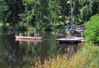 Bambini in canoa e un ragazzo che pesca dal molo al campeggio Le Paradou, Auvergne-Rhône-Alpes, Francia.