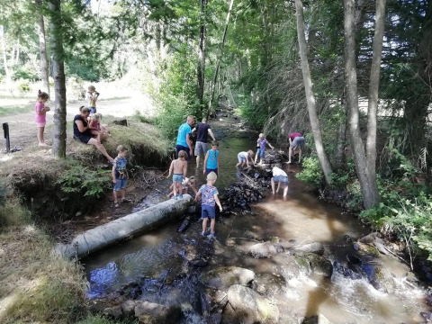 Bambini e adulti giocano e si rilassano presso un ruscello nel bosco al campeggio Le Paradou, Auvergne-Rhône-Alpes, Francia.