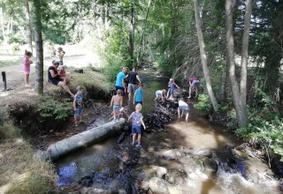 Bambini e adulti giocano e si rilassano presso un ruscello nel bosco al campeggio Le Paradou, Auvergne-Rhône-Alpes, Francia.