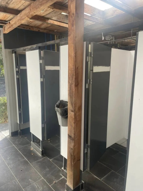 Bagni con divisori grigi e bianchi e cestino su palo in legno presso il campeggio Le Paradou.