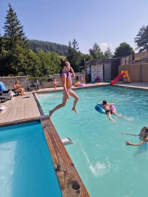 Bambina salta nella piscina al campeggio Le Paradou in Alvernia-Rodano-Alpi, Francia, tra la natura verde.