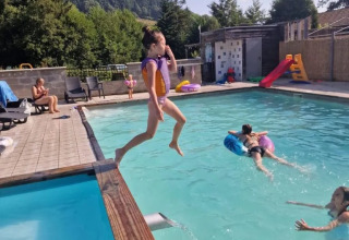 Bambina salta nella piscina al campeggio Le Paradou in Alvernia-Rodano-Alpi, Francia, tra la natura verde.
