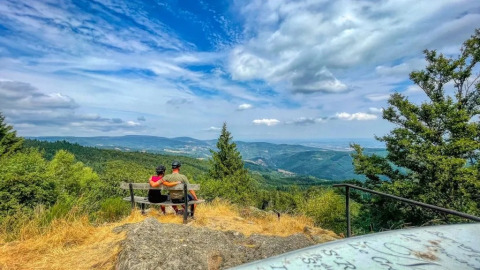 Coppia seduta su una panchina ammira il panorama collinare presso Saint-Priest-la-Prugne, Francia.
