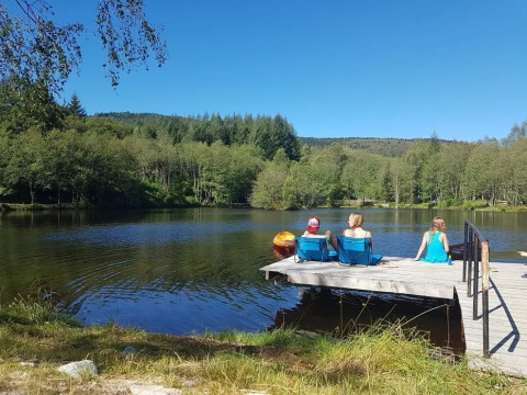 Tre persone si rilassano su un molo di legno presso il lago al campeggio Le Paradou in Alvernia-Rodano-Alpi, Francia.