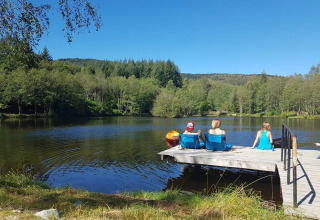 Tre persone si rilassano su un molo di legno presso il lago al campeggio Le Paradou in Alvernia-Rodano-Alpi, Francia.