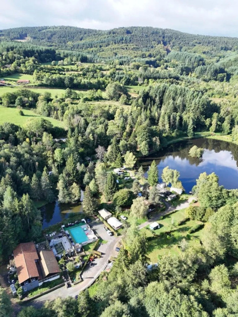 Vista aerea del Campeggio Le Paradou con piscina, lago, boschi e edifici in Auvergne-Rhône-Alpes, Francia.
