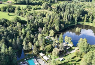 Vista aerea del Campeggio Le Paradou con piscina, lago, boschi e edifici in Auvergne-Rhône-Alpes, Francia.