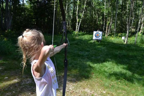 Una bambina mira con arco e freccia a un bersaglio al campeggio Le Paradou, Auvergne-Rhône-Alpes, Francia.