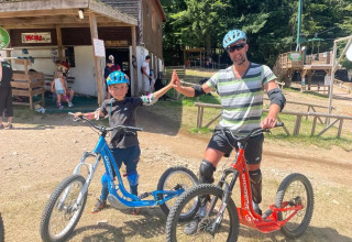 Due persone con casco e protezioni fanno un high five vicino a monopattini in un villaggio vacanze in Francia.