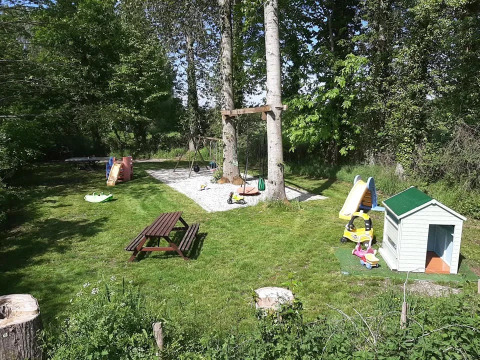 Area giochi al campeggio Le Bois Coudrais in Bretagna, Francia, con altalene, scivolo e casetta per bambini.