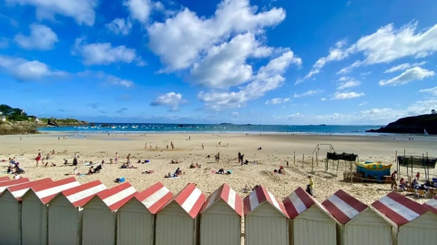 Spiaggia con cabine bianche e rosse, persone che prendono il sole vicino a Cuguen in Bretagna, Francia.