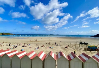 Spiaggia con cabine bianche e rosse, persone che prendono il sole vicino a Cuguen in Bretagna, Francia.