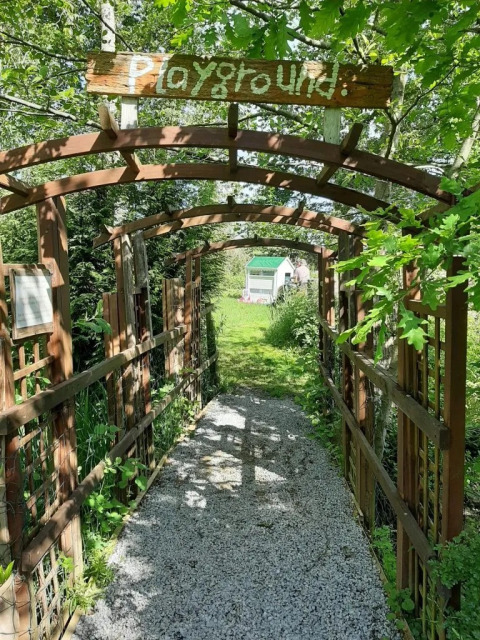 Ingresso al parco giochi nel campeggio Le Bois Coudrais in Bretagna, Francia, circondato dal verde.