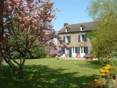 Casa in pietra al campeggio Le Bois Coudrais in Bretagna, Francia, circondata da alberi in fiore e giardino verde.