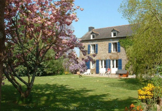 Casa in pietra al campeggio Le Bois Coudrais in Bretagna, Francia, circondata da alberi in fiore e giardino verde.