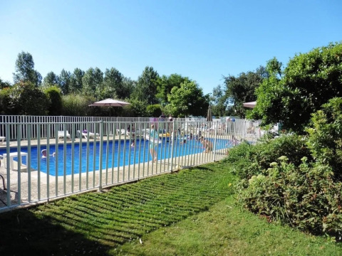 Piscina all'aperto con recinzione di sicurezza, sdraio e verde al campeggio Le Bois Coudrais in Bretagna.