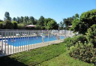 Piscina all'aperto con recinzione di sicurezza, sdraio e verde al campeggio Le Bois Coudrais in Bretagna.