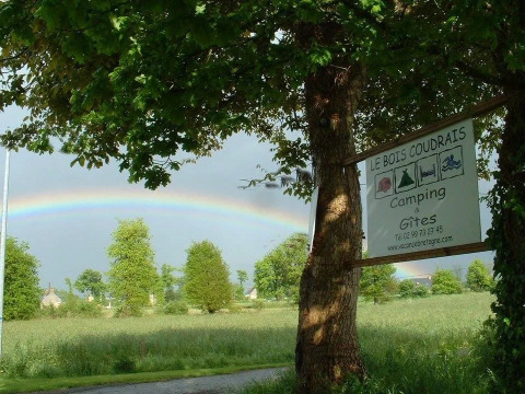 Arcobaleno sopra i campi verdi accanto al campeggio Le Bois Coudrais in Bretagna, Francia, con il cartello all’ingresso.